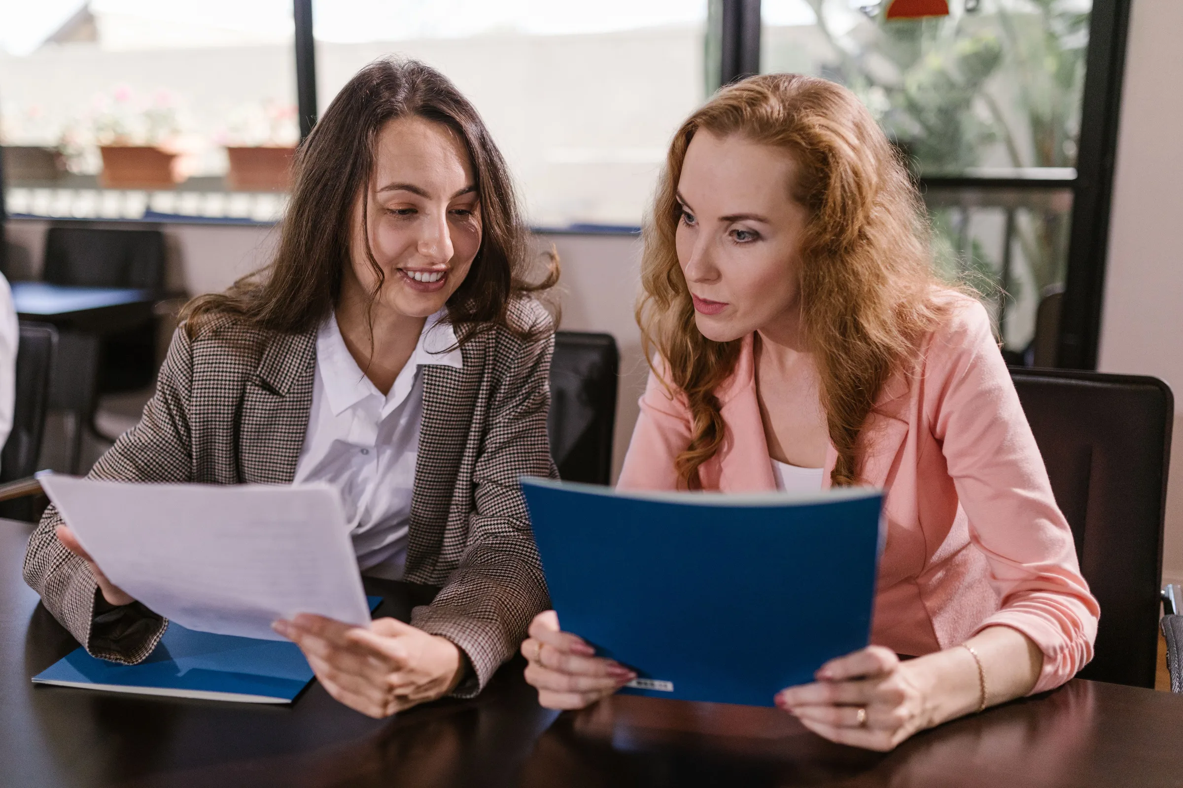 Two professionals reviewing printed documents together at a timber table in a plain meeting room