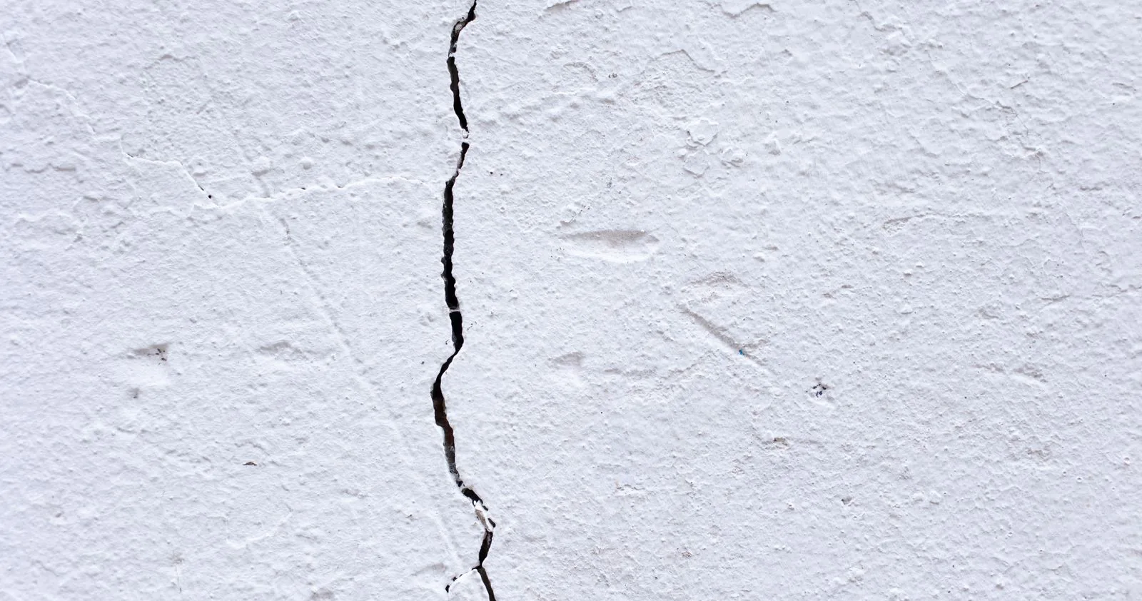 Close-up of a white rendered wall with one prominent vertical crack running its full height
