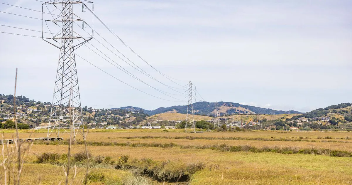 High-voltage transmission towers and power lines crossing open land, forming a wide electricity easement corridor